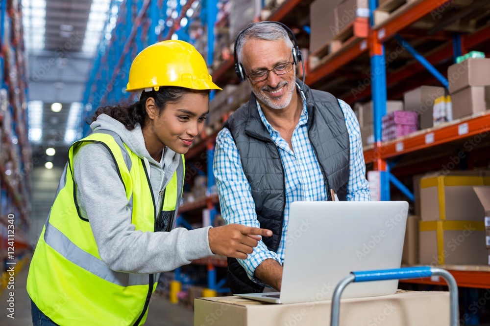 Warehouse manager and female worker using laptop Warehouse manager and female worker using laptop