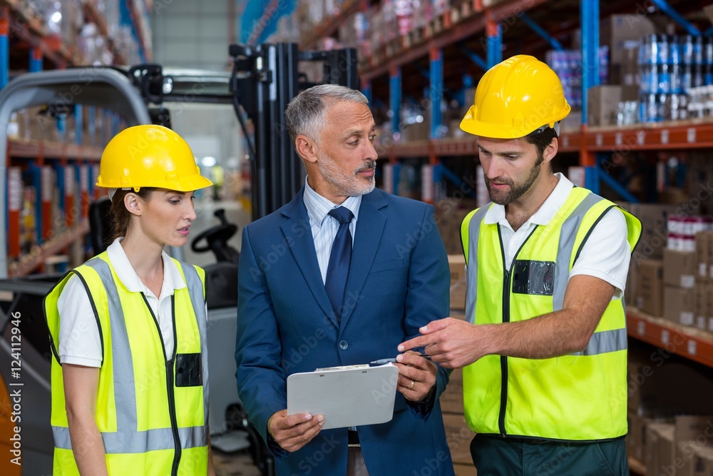 Warehouse manager and co-workers discussing over clipboard Warehouse manager and co-workers discussing over clipboard