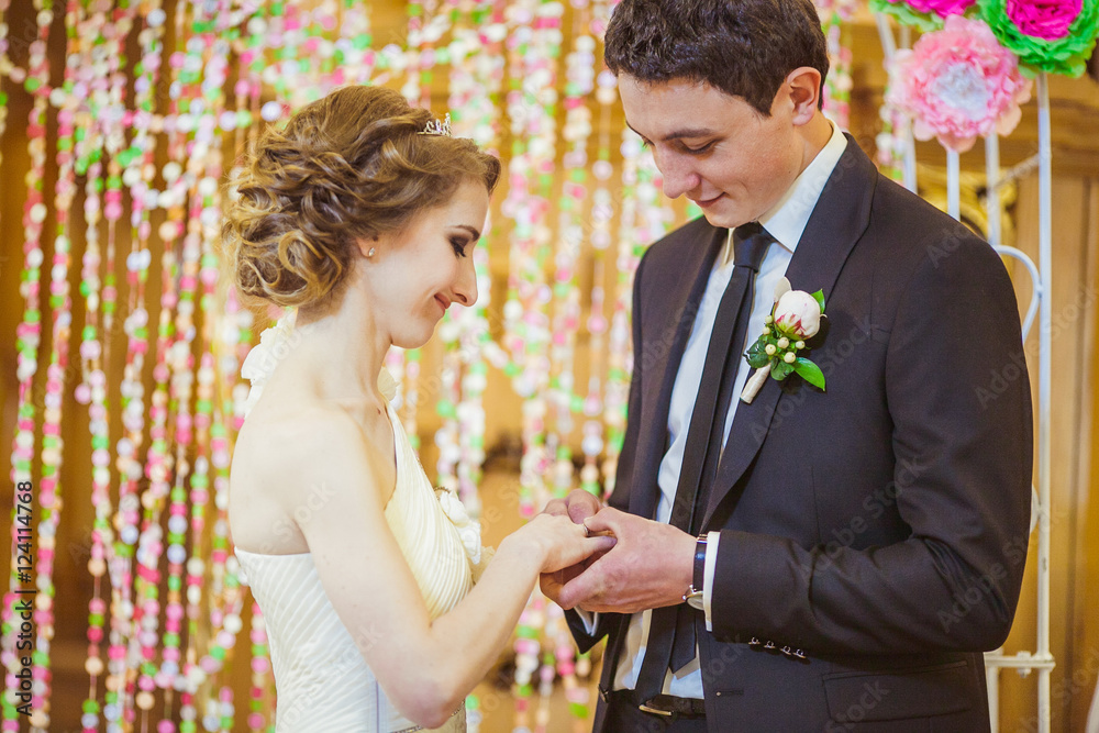 Handsome tall groom puts wedding ring on bride's hand