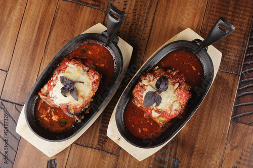 Baked zucchini and eggplant with tomato sauce in a pan. Wooden background.