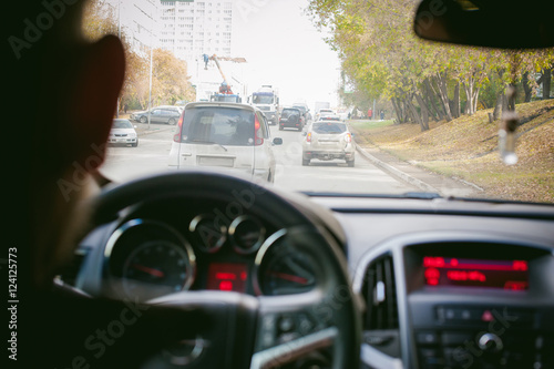 man drives a car. A guy in a jacket sits behind the wheel of a car traveling on the road in a traffic jam. Photo taken off the seat, due to the driver's back