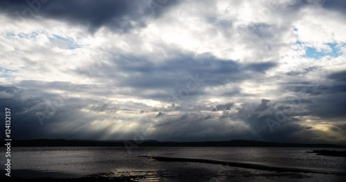 Sunbeams through moody clouds over water time-lapse