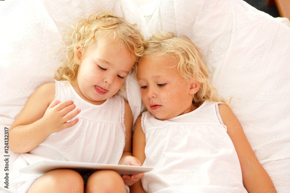 Innocent little sisters using digital tablet on bed Innocent little sisters using digital tablet on bed