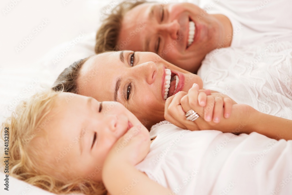 Cute little girl with her parents lying on bed Cute little girl with her parents lying on bed