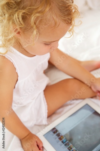 Cute little girl sitting on bed with digital tablet