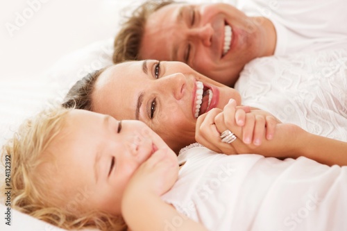 Cute little girl with her parents lying on bed