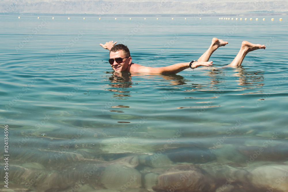 Man in sunglasses poses like airplane on surface Dead Sea. Free time, vacation, Wellness tourism, recreation concept.
