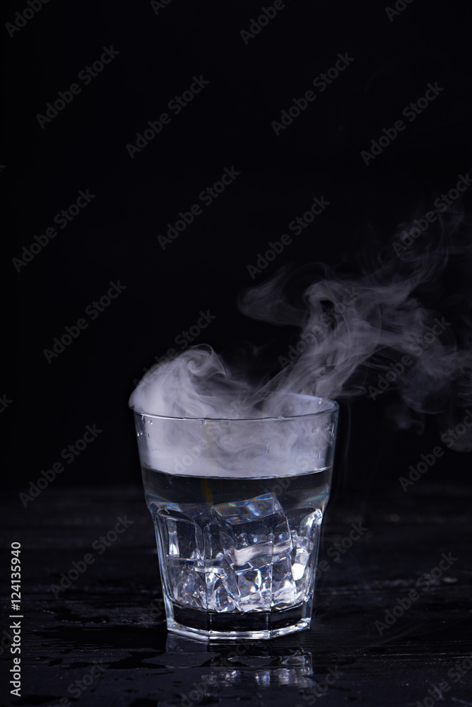 Hot water with a lot of steam in a glass at a black background. Dark ...