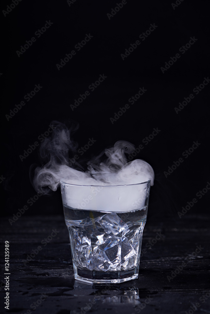 Hot water with a lot of steam in a glass at a black background. Dark ...