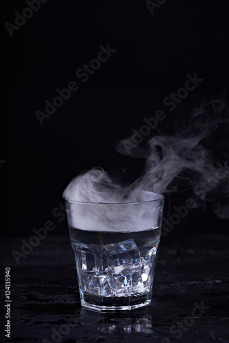 Hot water with a lot of steam in a glass at a black background. Dark photo. Concept photo: three state of water - ice, water, steam.