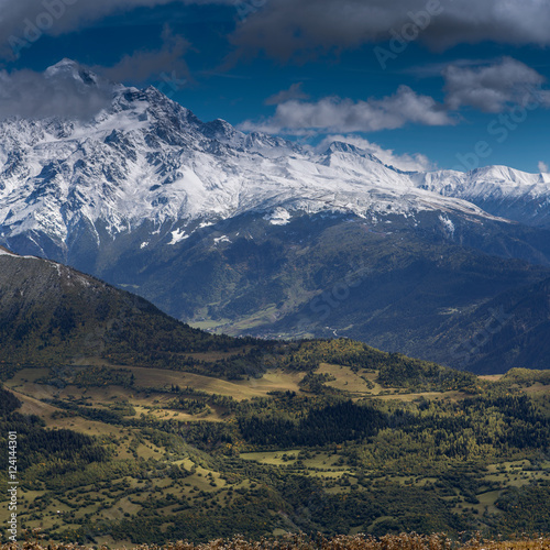 Mountain panorama with a green field slope, wooded mountains and snowbound peaks in the background. Svaneti, Georgia © uiliia
