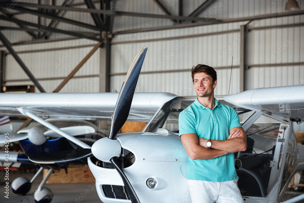 Man standing with arms crossed and smiling near small plane Man standing with arms crossed and smiling near small plane