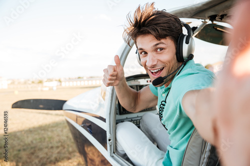 Canvas-taulu Cheerful pilot sitting in airplane cabin and showing thumbs up