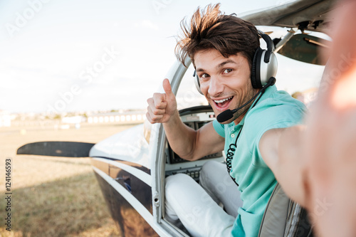 Cheerful pilot sitting in airplane cabin and showing thumbs up photo