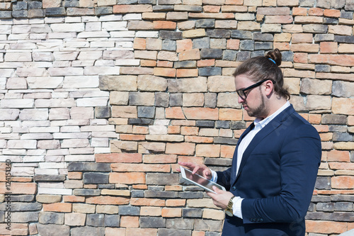 Young man wearing glasses using tablet computer on a brick wall background