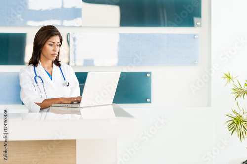 Attractive young female woman Latin Hispanic doctor nurse practioner in hospital clinic medical center office with laptop photo