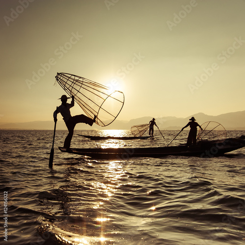 Burmese fisherman on bamboo boat catching fish in traditional way with handmade net. Inle lake, Myanmar (Burma) travel destination