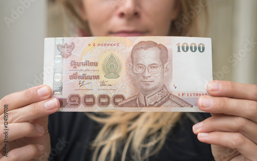 Closeup of 1000 Thai Baht note withdrawned from ATM over blurred woman's face