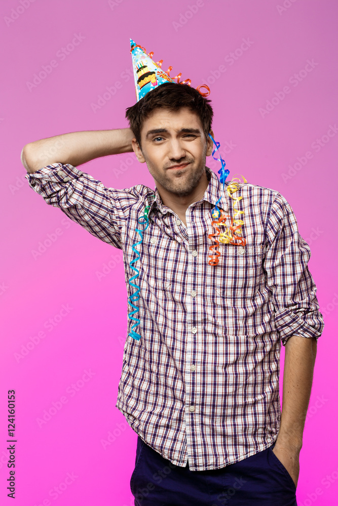 Displeased tired man at birthday party over purple background.