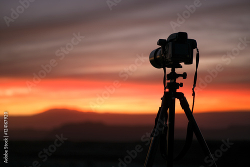 Camera set on a tripod aimed at a silhouette of a landscape during sunset photo