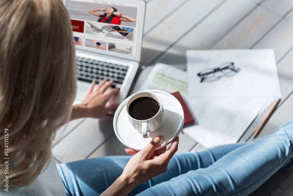 Close up of woman holding coffee cup and using laptop - obrazy, fototapety, plakaty 