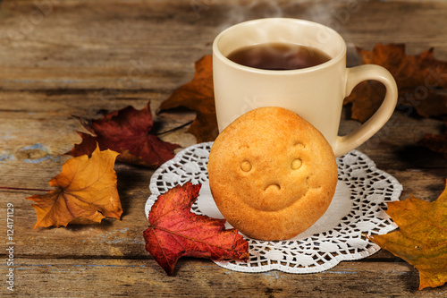 Hot drink and biscuit with a smile and autumn leaves on a wooden table surface