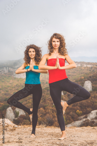 Two girls are doing yoga in mountains landscape
