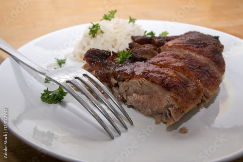 fried duck breast and rice with parsley garnish and a fork on a white plate