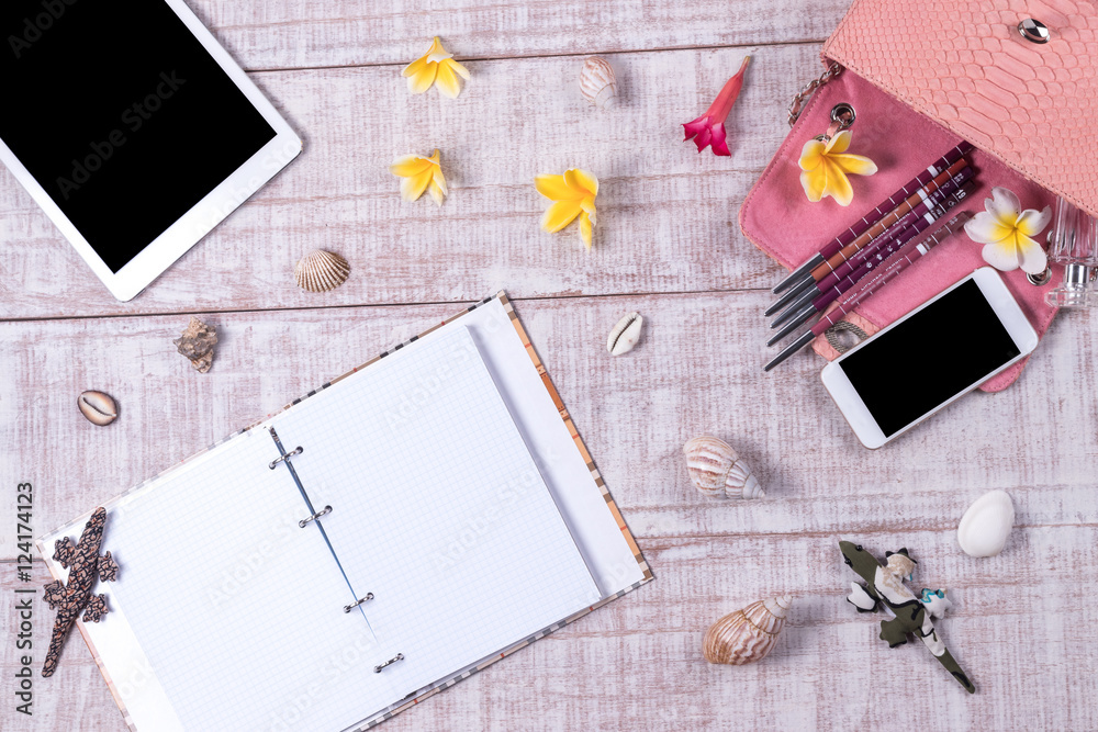 Overhead of a essentials objects in a fashion blogger. Top view of fashion python snakeskin handbag, smartphone, tablet pc, shells. Plumeria frangipani flowers. Wooden background. Notebook.