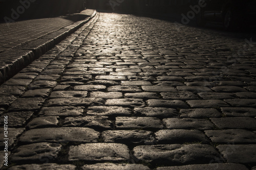 Fotografiet Black cobbled stone road background with reflection of light seen on the road