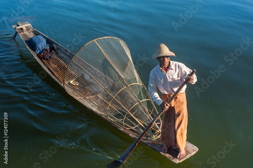 Burmese fisherman on bamboo boat catching fish in traditional way with handmade net. Inle lake, Myanmar (Burma) travel  destination