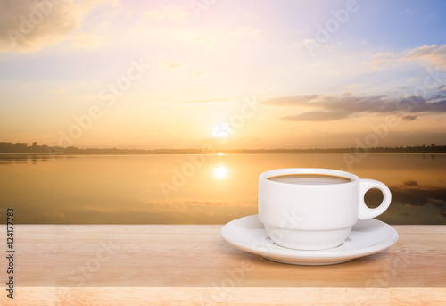 white coffee cup on wood table and view of sunset in the river background