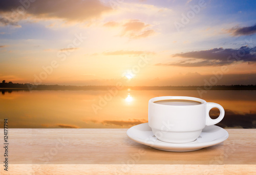 white coffee cup on wood table and view of sunset in the river background