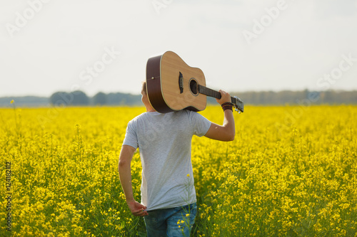 gay single man plays guitar in a field.