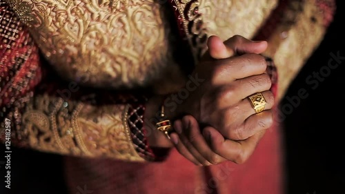 Indian man holds his hands together standing in wedding suit