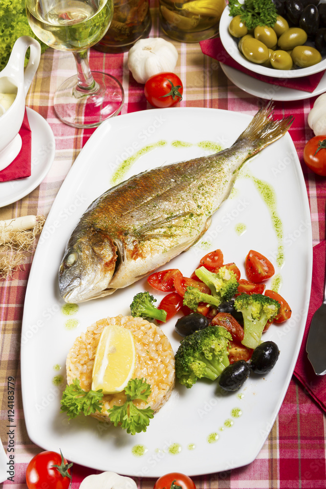 Fried gilt-head bream on a plate with a side dish of broccoli, cherry tomatoes, rice, olives and lemon. Fried gilt-head bream on a plate with a side dish of broccoli, cherry tomatoes, rice, olives and lemon.