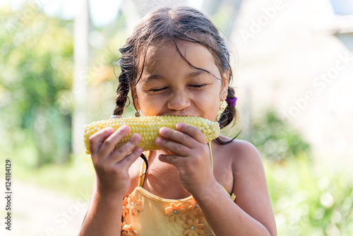 Child in the garden - lovely girl eating corn on the cob (GMO free).
