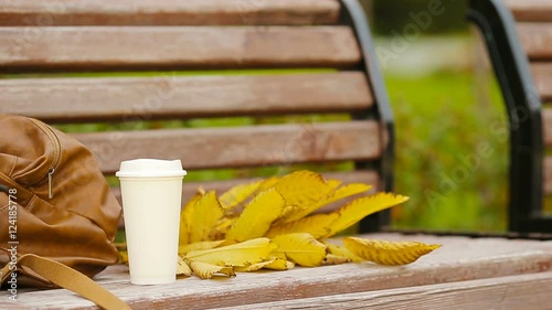 Cup of hot coffee and yellow autumnal leaveas on the park bench photo