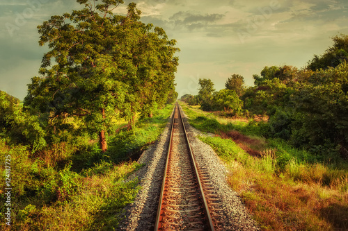 Railway track crossing rural landscape under evening sunset sky. Travel concept in vintage style