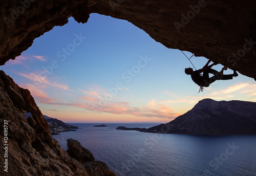 Male climber climbing along roof in cave at sunset