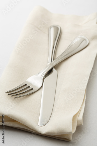 Simple, classic table setting place setting with fork and knife on white linen napkin. Selective focus on tines of fork.