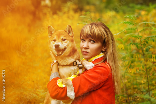 Girl hugs a dog Shiba Inu in autumn park.