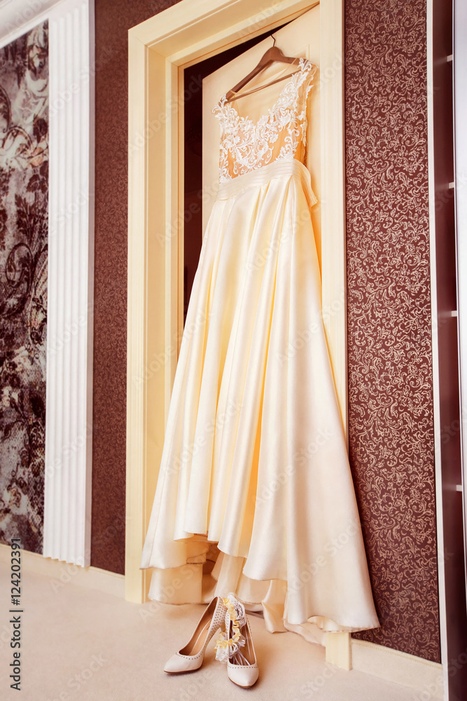 White luxury bridal dress is hanging on door at wall background White luxury bridal dress is hanging on door at wall background