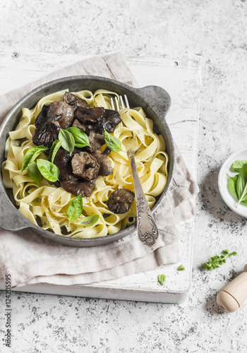 Italian pasta tagliatelle with wild mushrooms in a frying pan on a light background. Delicious vegetarian food