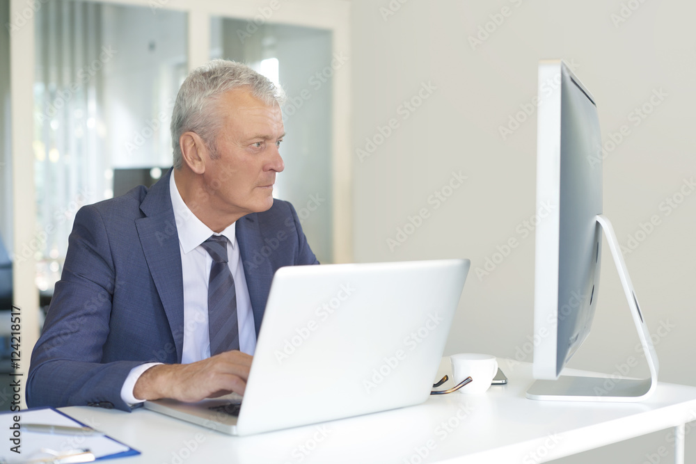 Financial businessman at work. Shot of a senior financial manager working at office in front of laptop and and doing some paperwork. Financial businessman at work. Shot of a senior financial manager working at office in front of laptop and and doing some paperwork.