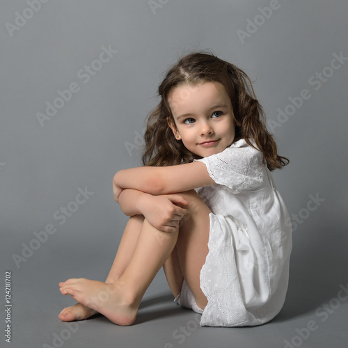 Fotografi Sweet little happy girl in white dress, studio portrait over gra