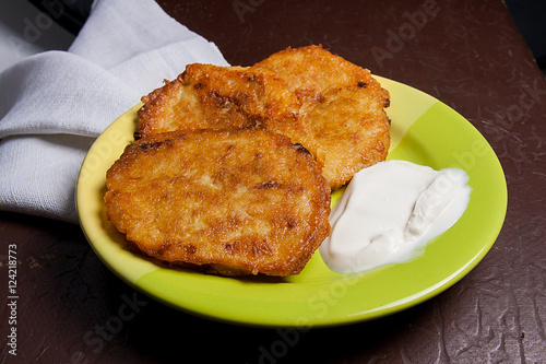 Potato pancakes with meat and sour cream on green plate in Belar