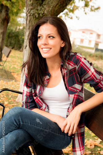 Beautiful young woman sitting in park at fall