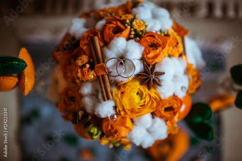 Golden rings lie on the bouquet made of orange flowers and cotto