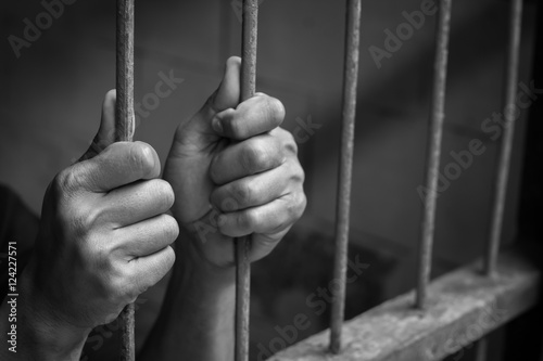Soft focus on hands of man behind jail bars. vintage or retro style. selective focus. black and white image.